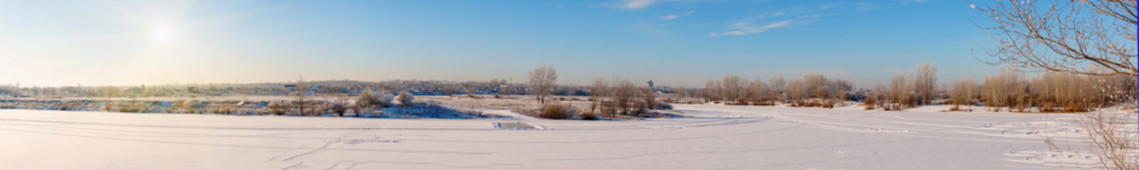 Fototapeta na wymiar Winter landscape panorama. A winter river and a village in the distance covered with snow