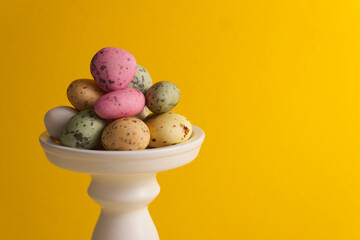 Colored and spotted candies sea stones on a white stand on a yellow background close-up