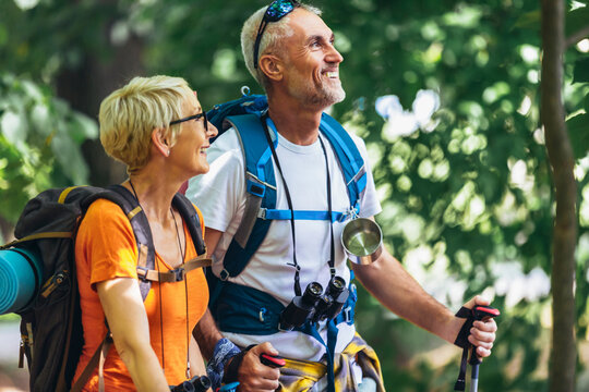 Mature couple hiking in forest wearing backpacks and hiking poles. Nordic walking, trekking. Healthy lifestyle.