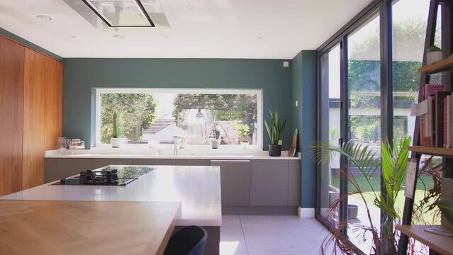 Camera tracks interior of beautiful contemporary kitchen with fitted appliances and storage with views to garden - shot in slow motion