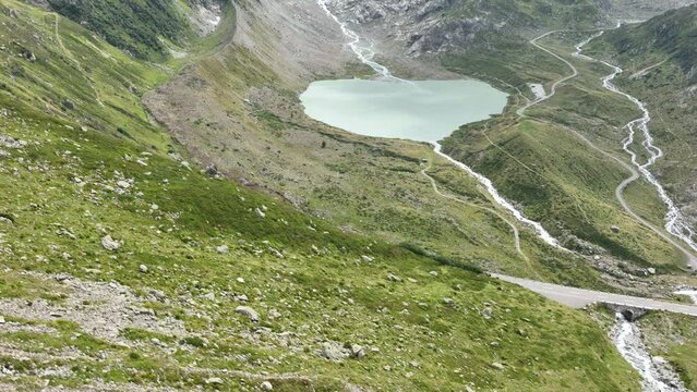 Mountain lake called the Steinsee on top of the Sustenpass in Switzerland. Aerial overhead view. Driving road, rocks, grass, moss and mountain landscape.