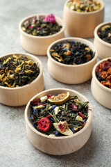 Different kinds of dry herbal tea in wooden bowls on light grey table