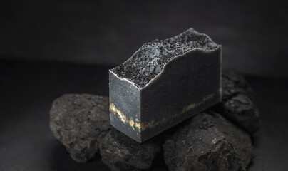 Piece of natural charcoal soap on real coals on a black background. Concept of making and using organic eco soap and cosmetics