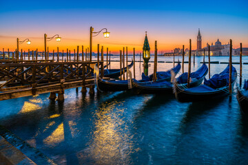 Naklejka premium Long exposure: Gondolas floating by the shoreline of San Marco Square at sunrise in front of the Island of San Giorgio Maggiore in Venice, Italy