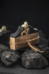 Piece of natural charcoal soap wrapped with craft paper and rope on coals on a black background. Concept of making and using organic soap and cosmetics, eco handmade presents
