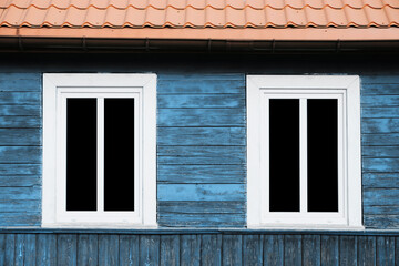 White PVC window background. Empty copy space rustic cottage house. Vintage cabin blue peeling paint wall. Countryside architecture texture. Red tile roof. Two windows next to each other.
