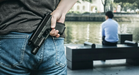 A man pulls out a gun rear view with blurred victim sitting beside river background, a concept of...