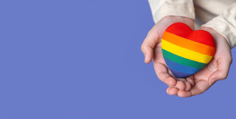 Close up rainbow heart in child's hands.  Top vıew Banner copy space for design text advertisement over purple blue background. Health insurance, donation charity, world heart day, appreciation