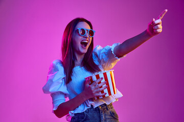 Excited movie. Portrait of young emotive girl posing in 3D glasses with popcorn basket over pink...
