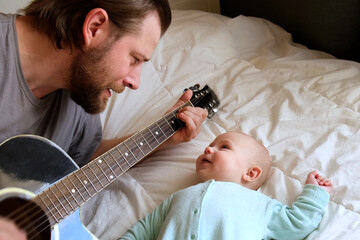 Bearded Father Playing Guitar to his Little Child. Baby Looking at Him, Listening and Smiling....