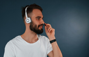 In headphones. Handsome man is in the studio against blue background