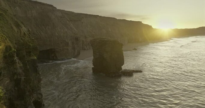 Rock pinnacle at New Zealand Fortrose cliffs during bright sunrise, aerial