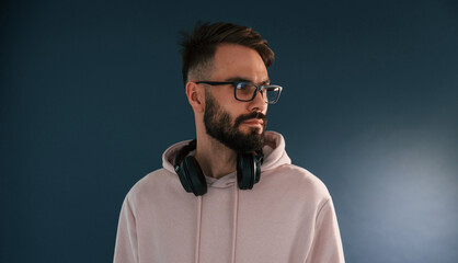 In glasses and with headphones. Handsome man is in the studio against blue background