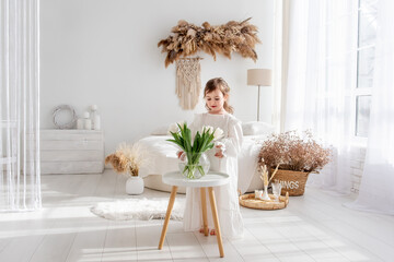 Little girl in a white dress, nightgown. Toddler collects bouquet of fresh, delicate white tulips
