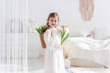 Close-up portrait of a little girl in a white dress, nightgown. Toddler embraces a bouquet of...