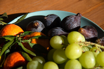 Different organic fruits from local farmer market on plate on old wooden surface. Closeup. Seasonal fruit background. Healthy eating, simple lifestyle in country home concepts. Selective focus on figs