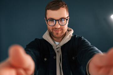 Making selfie. Handsome man is in the studio against blue background