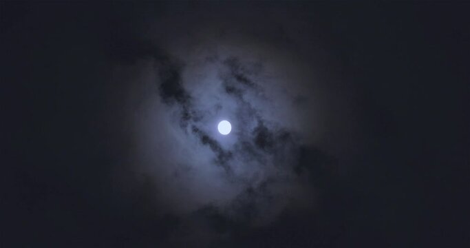 Full moon behind clouds. Full moon. The movement of the clouds against the background of the full moon