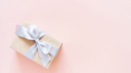 Rectangular gift box with silver ribbon on plain light pink background	