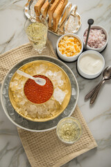 Orange Keta Lachs Kaviar in Dose auf Eis in Glas Schale mit Perlmutt Löffel, Sekt Champagner, gekochte Eier Würfel, Charlotten Zwiebel Würfel, Toast Brot und Saure Sahne auf Serviette und Marmor hell