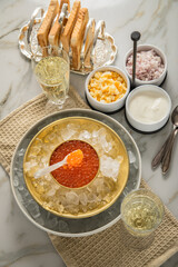 Orange Keta Lachs Kaviar in Dose auf Eis in Glas Schale mit Perlmutt Löffel, Sekt Champagner, gekochte Eier Würfel, Charlotten Zwiebel Würfel, Toast Brot und Saure Sahne auf Serviette und Marmor hell
