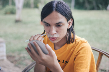 Peruvian queer person applying make-up outdoors 

