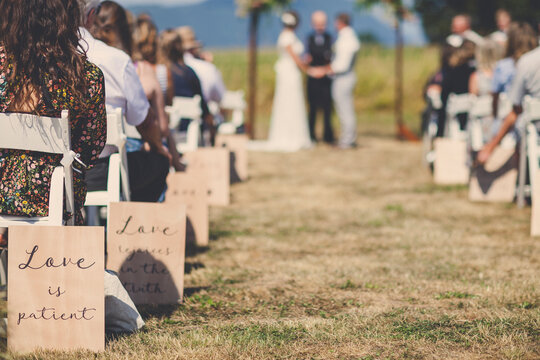 People sitting while young couple getting married by priest during sunny day