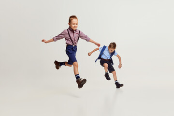 Joyful boys, children in stylish classical clothes playing together, running, jumping over grey studio background. Concept of game, childhood, friendship