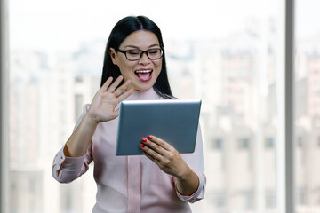 Fototapeta premium Young asian businesswoman to someone via tablet pc. Blurred windows backgorund.