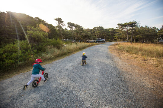 Rear view of brother and sister biking on gravel road at dawn.