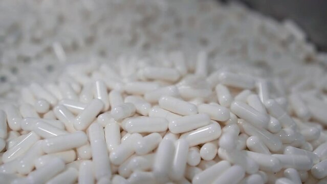 recopilaci&oacute;n de c&aacute;psulas blancas cayendo en recipiente de industria farmac&eacute;utica.