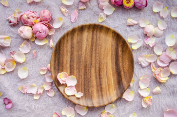 Pink and yellow rose petals and rosebuds and wooden plate on knitted pink background. Natural...