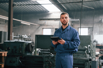 Working by using digital tablet. Man at the factory that is in blue uniform is indoors