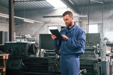 Working by using digital tablet. Man at the factory that is in blue uniform is indoors