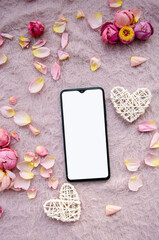 Digital smartphone, blank screen with small petals and white tangled hearts on pink knitted background.Valentines Day background and Copy space for your text.
