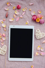 Digital tablet, blank screen with small petals and white tangled hearts on pink knitted background.Valentines Day background and Copy space for your text.