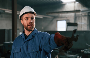Wrench in the hand. Factory worker in blue uniform is indoors
