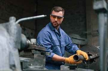 In protective wear. Operating machine. Factory worker in blue uniform is indoors