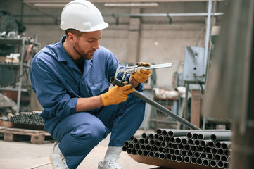 Measures the diameter of a metal pipe. Factory worker in blue uniform is indoors