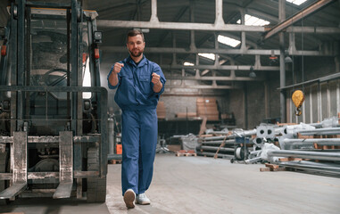 Fototapeta na wymiar With the forklift. Factory worker in blue uniform is indoors