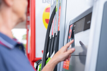 Woman at self-service fuel pump in European gas station types on the display the required amount -...
