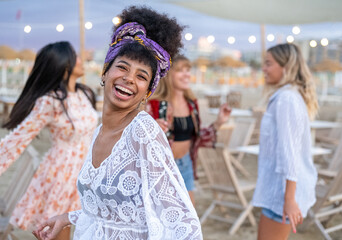 Attractive woman in stylish dress dancing on the beach, African woman smiling and  having fun at beach party with friends, women on luxury travel and holidays, resort lifestyle