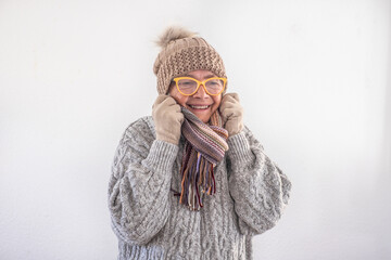 Smiling elderly senior woman in gray sweater with glasses and cap covers her neck because she feels cold, isolated on white background