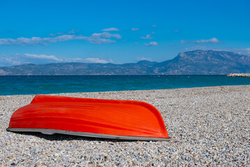 Overturned red row boat lying on the pebble beach near by the Aegean sea