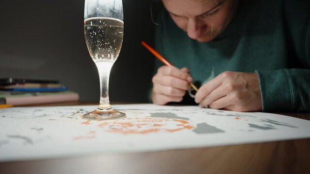A girl with a glass of champagne on the table draws a picture