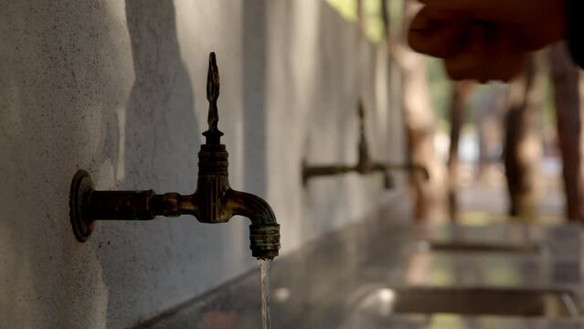 Rack focus man hand open flowing water from three faucets and begin senseless consumption and waste of water to nowhere. not caring for environment. Opening tap with running cold water in nature