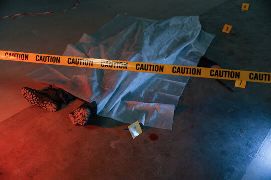 Knife and blood. Dead body of a man is on the ground, covered in white cloth. Conception of murder, homicide