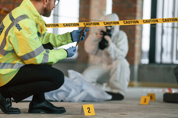 Woman is using camera, making photos. Detectives are collecting evidence in a crime scene near dead body