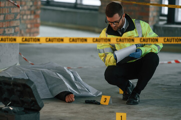 Notepad with information. Male detective is collecting evidence in a crime scene near dead body on the construction site