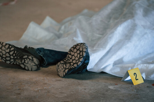 Dead body of a man is on the ground, covered in white cloth. Conception of murder, homicide